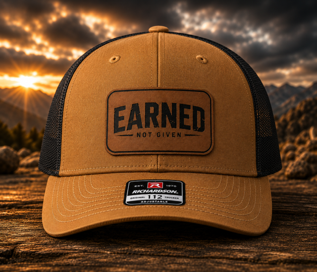 Carmel/Black mesh-back trucker hat with a rawhide leatherette patch engraved with the Earned Not Given design.