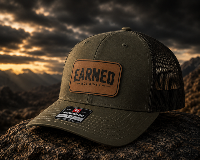 Green mesh-back trucker hat with a rawhide leatherette patch engraved with the Earned Not Given design.